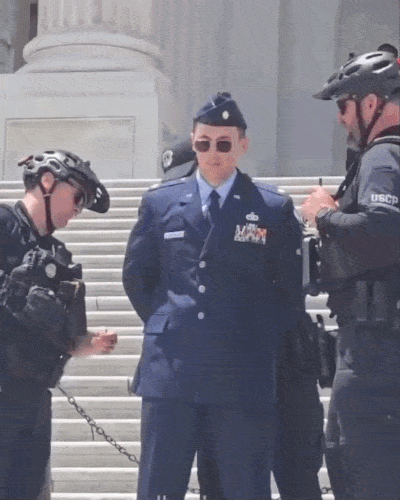 Major Jason Watson is arrested on the Capitol steps Overlaid with a cross of type that says 'free major Watson'